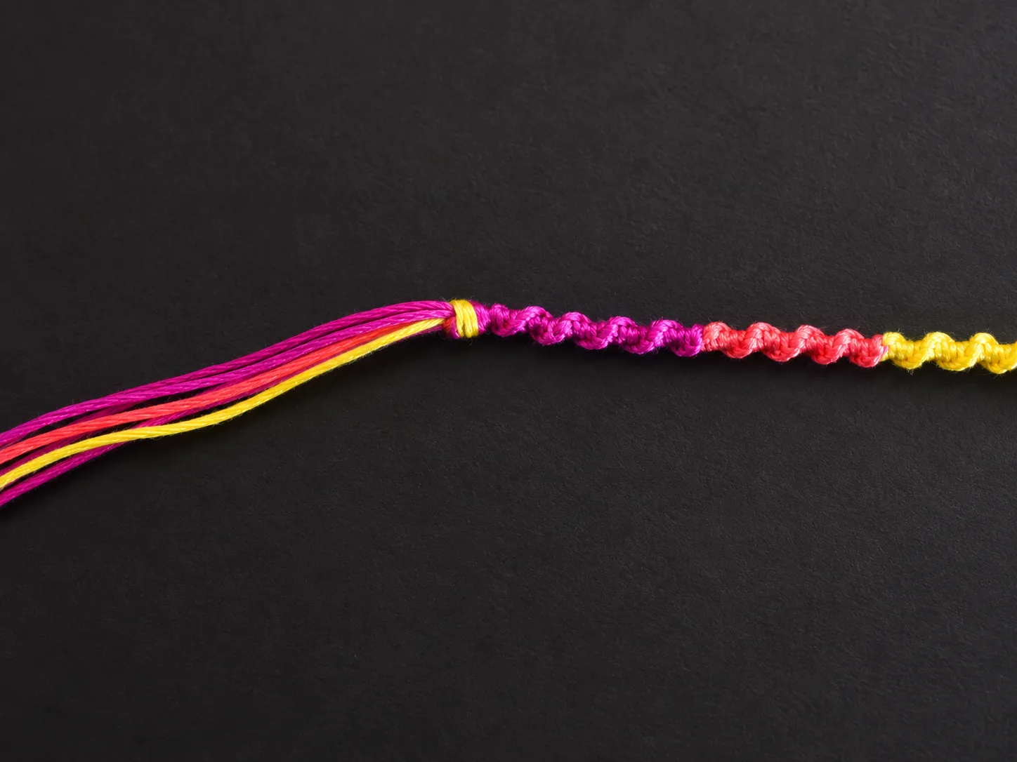 Nearly finished spiral friendship bracelet with loose embroidery floss ends ready for finishing