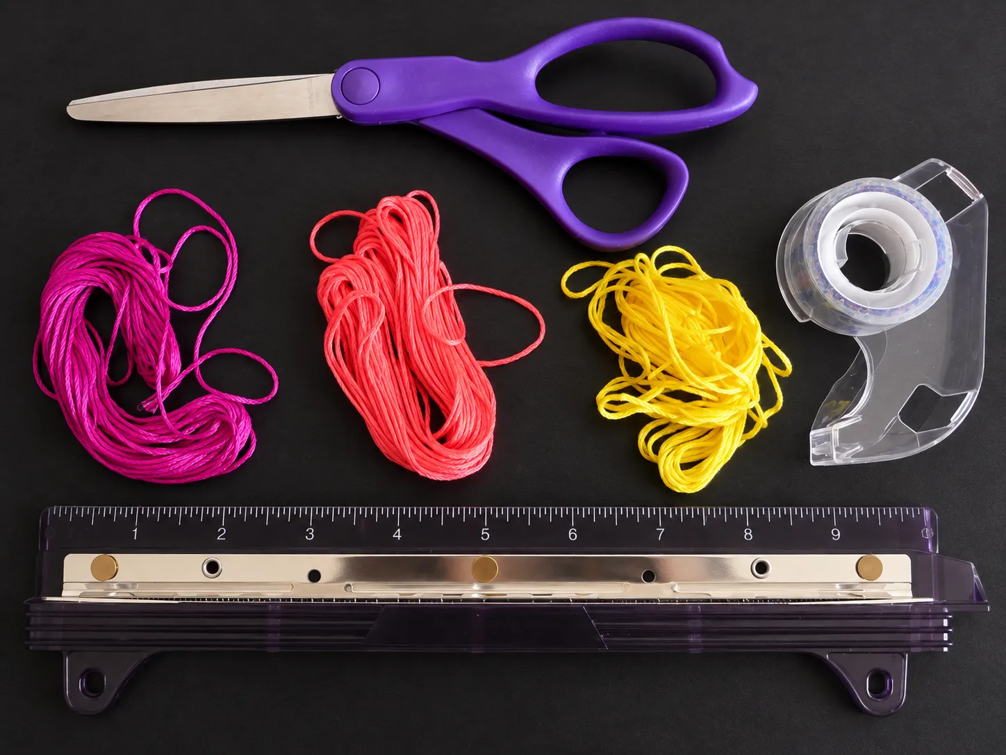 Materials for making an easy spiral friendship bracelet including embroidery floss, scissors, tape, and ruler